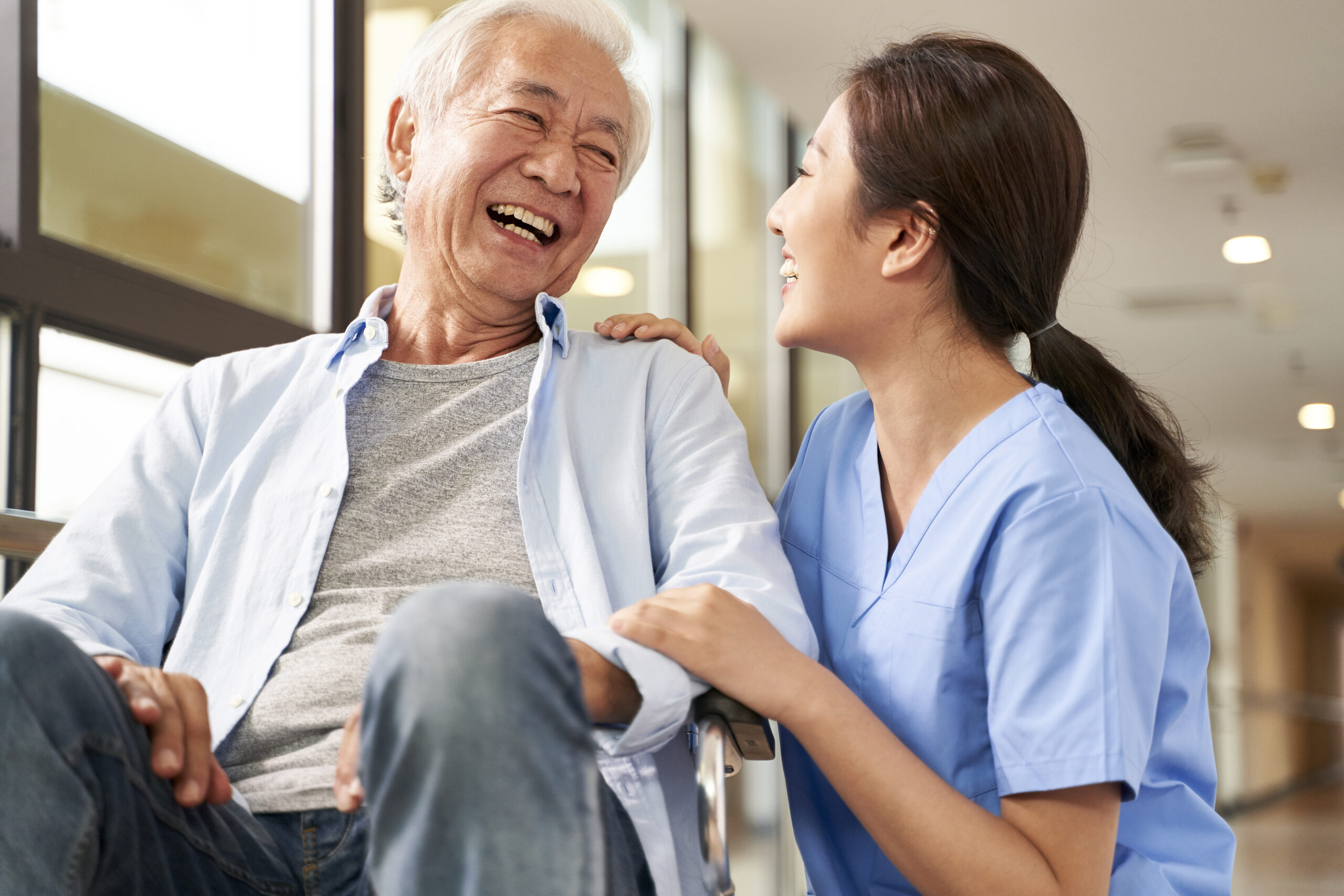 friendly asian caretaker talking to senior patient in nursing home senior living technology for COVID-19