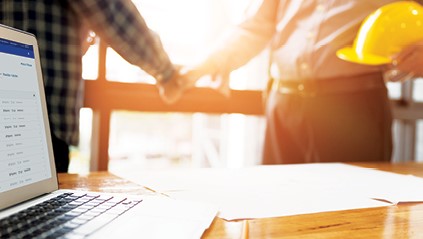 two men shaking hands in front of table with laptop