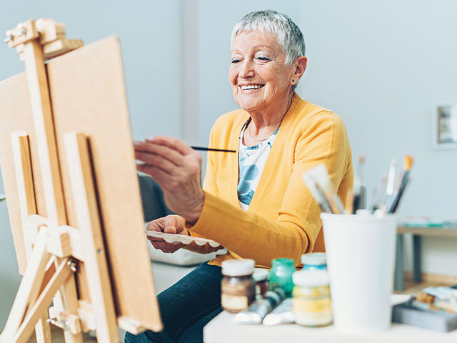 senior woman in yellow sweater painting at her desk